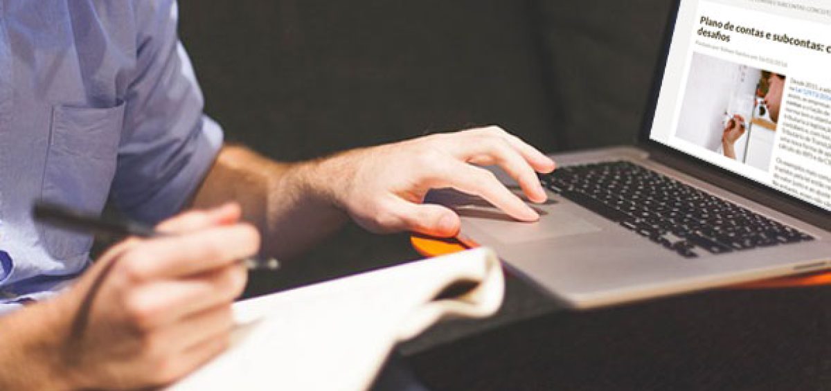 Homen digitando em notebook e fazendo anotações em caderno enquanto pesquisa sobre plano de contas contábil, destacando pontos de atenção na governança fiscal e tributária