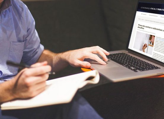 Homen digitando em notebook e fazendo anotações em caderno enquanto pesquisa sobre plano de contas contábil, destacando pontos de atenção na governança fiscal e tributária