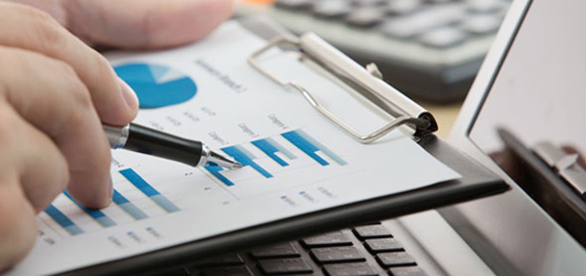 Profissional analisando gráficos financeiros em relatório impresso sobre notebook, representando os impactos da moeda funcional no SPED Contábil e na gestão tributária empresarial.