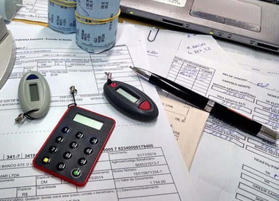 Riscos do registro de moeda funcional no programa SPED Contábil com documentos fiscais, calculadora e tokens de segurança em mesa de escritório