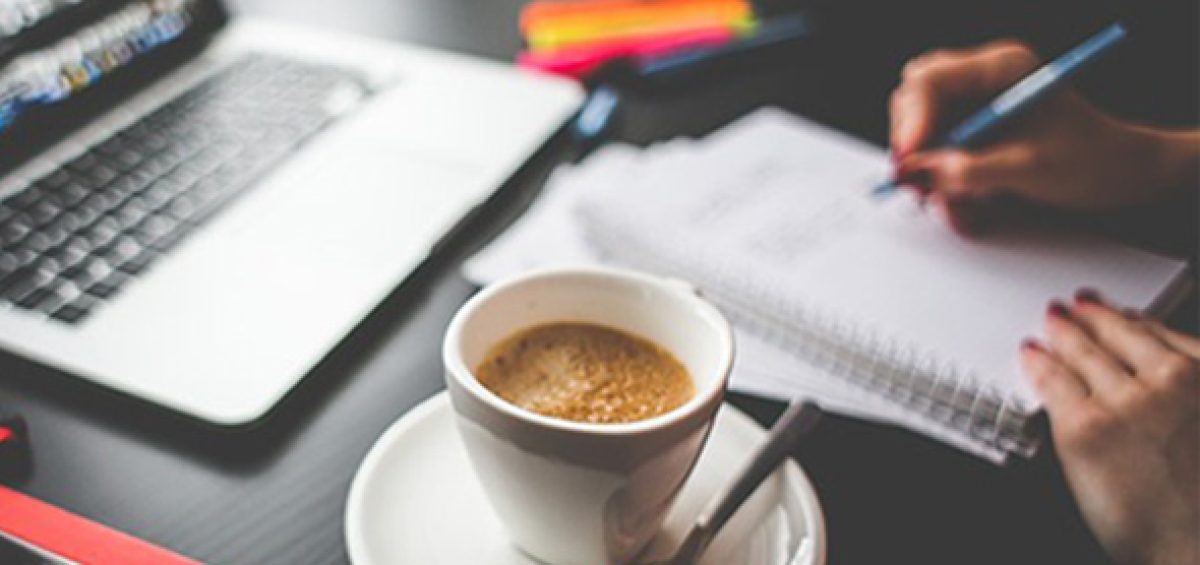 Pessoa em ambiente de trabalho escrevendo em caderno ao lado de notebook e café, representando treinamento sobre regime de drawback via e-mail para gestão eficiente e geração de resultados.