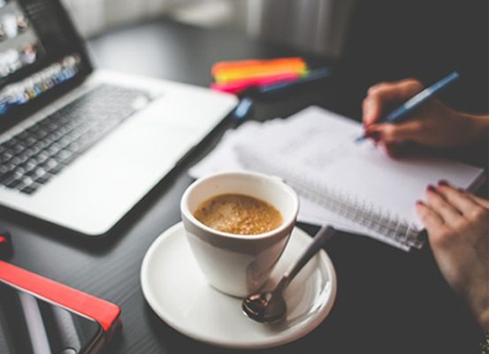 Pessoa em ambiente de trabalho escrevendo em caderno ao lado de notebook e café, representando treinamento sobre regime de drawback via e-mail para gestão eficiente e geração de resultados.