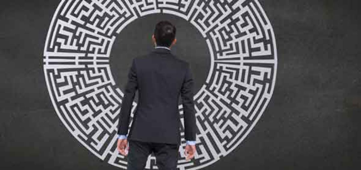 Homem de terno observando um labirinto circular em parede escura, simbolizando os desafios e oportunidades na gestão de regimes especiais para redução de custos empresariais