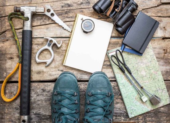 Equipamentos de alpinismo e planejamento organizados em mesa de madeira com botas, bússola, mapa e caderno, simbolizando preparo e profissionalismo na entrega da ECF