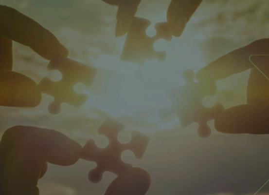 Mãos unindo peças de quebra-cabeça ao pôr do sol, representando estratégias tributárias colaborativas que agilizam o retorno do crescimento da indústria
