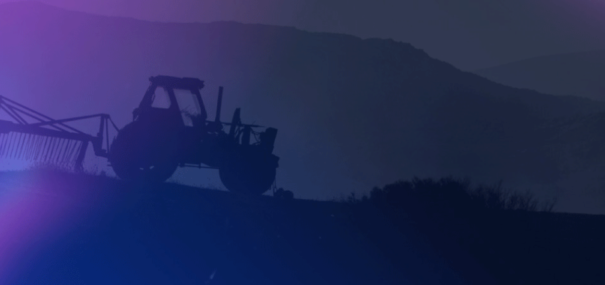 Silhueta de um trator agrícola autopropulsado ao entardecer, com montanhas ao fundo e iluminação em tons de roxo e azul. Representação dos desafios e perspectivas do setor de máquinas agrícolas.
