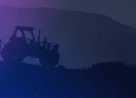 Silhueta de um trator agrícola autopropulsado ao entardecer, com montanhas ao fundo e iluminação em tons de roxo e azul. Representação dos desafios e perspectivas do setor de máquinas agrícolas.