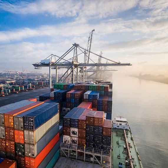 Navio cargueiro em porto com contêineres coloridos e guindastes, representando a gestão da exportação indireta e processos logísticos internacionais.