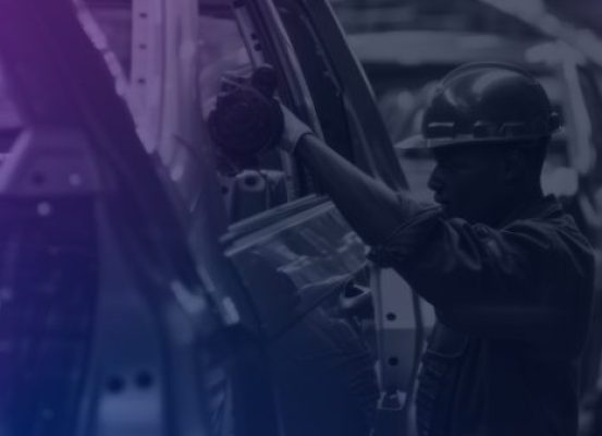 Trabalhador em uma linha de montagem industrial, utilizando equipamentos de proteção enquanto realiza a montagem da carroceria de um automóvel em uma fábrica, simbolizando a crescimento na produção de autoveículos em 2025.